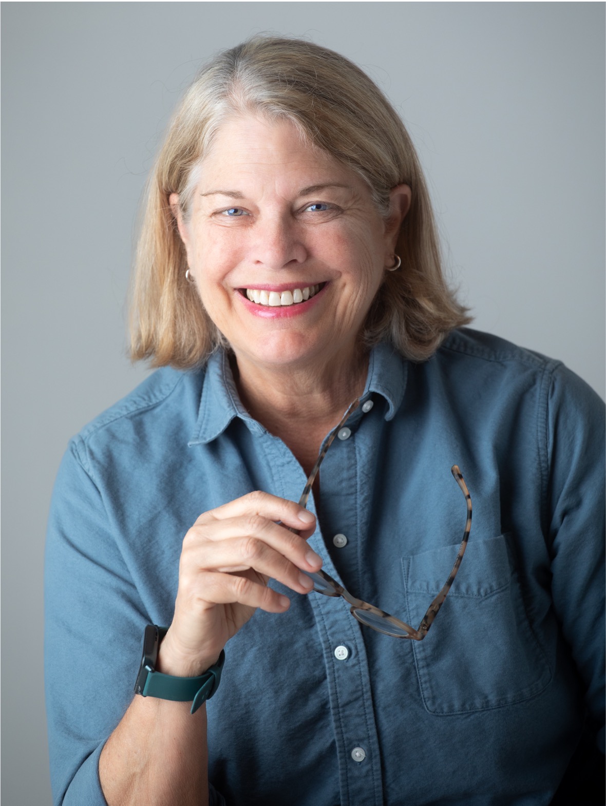 Alison Head - woman with short blond hair, smiling, holding glasses in right hand